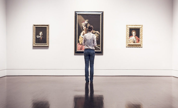 Une femme observe trois peintures dans un musée