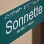 Un panneau avec les mentions "Sonnette" et "rendez-vous" écrits. Elles ont aussi été mises en braille.